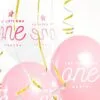 Balloons с надпис "1st BIRTHDAY ONE PARTY", празнична украса за първи рожден ден, розови и бели балони, със златни и сребърни декоративни ленти, весела атмосфера за детски тържества.
