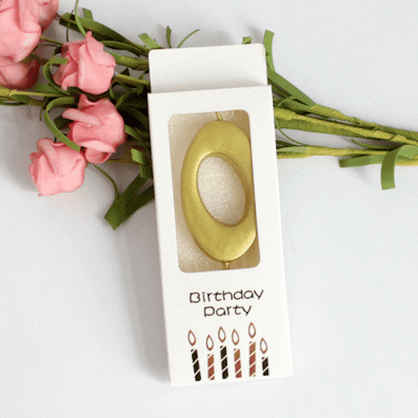 Златист рожден ден свещ в опаковка с цветя и надпис "Birthday Party" за празнична декорация и торта.
