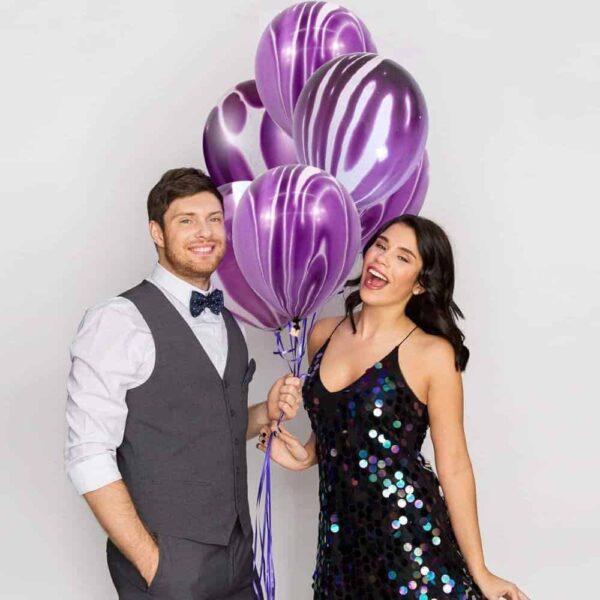 Участници в празнична снимка с лилави балони, носещи елегантни облекла и усмихващи се на камерата, идеални за събития и партита.