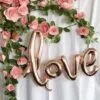 Златисти балони със формата "love" и розови рози, идеални за романтични празници и сватби.