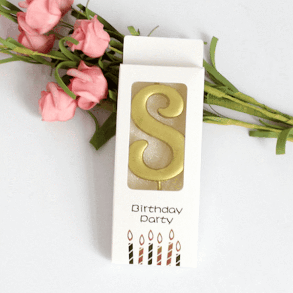 Златна свещ във форма на буква "S" за рожден ден или парти, красиво опакована с цветя за празнична атмосфера. Перфектна декорация за специален повод.