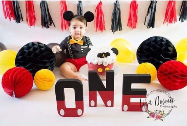 Момиченце на детска рожден ден с черно, бяло, жълто и червено декор, балони и торта, свързани с themes на Мики Маус.