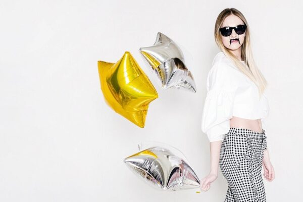 Златни и сребърни балони за парти с жена в стил ретро, носеща черни очила и бяла риза, подходящи за тематични празненства и събития, организирани от Party Deluxe.