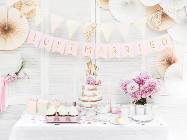 Лента с надпис "Just Married" и цветни декорации за сватбена парти, торта с розови цветя и десерти, създаващ перфектната атмосфера за празник на любов и съвместен живот.