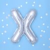 Метален балон във формата на буква X на светлосин фон с бели и сребърни конфетти за празненство.