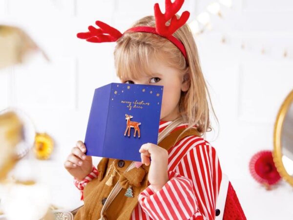 Коледна картичка с еленче и послание за мечти, детска ваканционна украса и бял фон, създаваща празнична атмосфера за Коледа и Нова година.