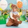 Катерична снимка на малко дете, участващо в празнична украса с големи балони и цветя, подготвено за детско парти с цветна и весела атмосфера.