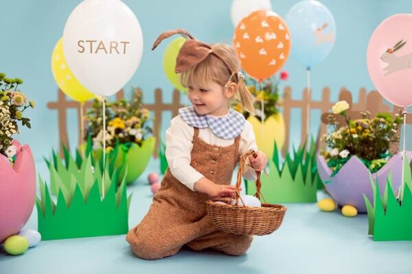 Катерична снимка на малко дете, участващо в празнична украса с големи балони и цветя, подготвено за детско парти с цветна и весела атмосфера.