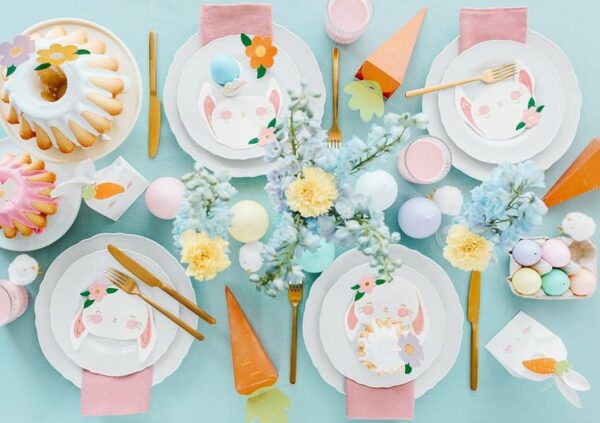 Pink Easter table setting with bunny-themed plates, colorful eggs, and spring flowers for festive celebrations.