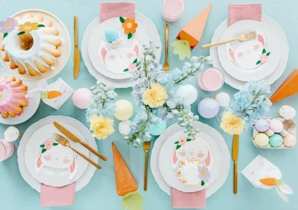 Pink Easter table setting with bunny-themed plates, colorful eggs, and spring flowers for festive celebrations.