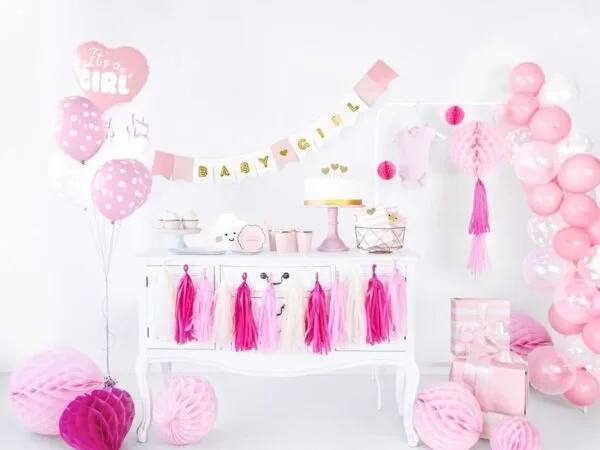 Pink baby girl celebration decorations with balloons, banner, cake, and gifts for a baby shower or first birthday party.