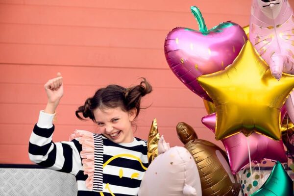 Ярка снимка на щастливо дете с балони за рожден ден, празнуващо и радостно в празнична атмосфера с ярки цветове и весел настроение.