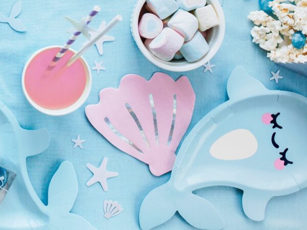 Въпросното изображение показва ярка морска тематична празнична маса с децки чинийки, сладкиши и морски декорации за парти.