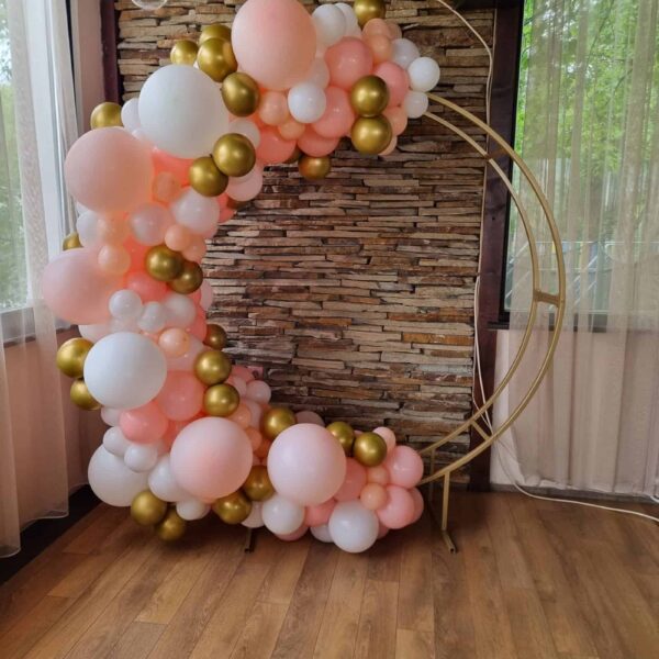 Розово-бели балони с златисти акценти, оформени във формата на полумесец, подходящи за празнична фотосесия или декорация за специални събития.