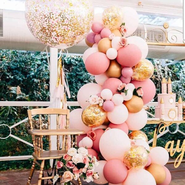 Цветна балонна украса за парти с розови, бели и златисти балони, цветя и тематична декорация, създаваща празнична атмосфера за специален повод.