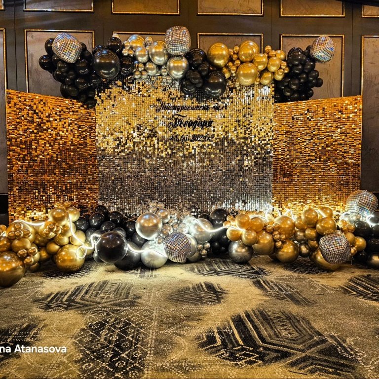 Бляскава декорация за празненство с балони в злато, черно и сребро, елегантен заден фон с мозаечни елементи, великолепна атмосфера за тържество или специален повод.