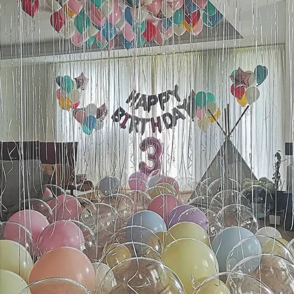Таван, покрит с пастелни балони с дълги панделки, гирлянд Happy Birthday и цифра три
