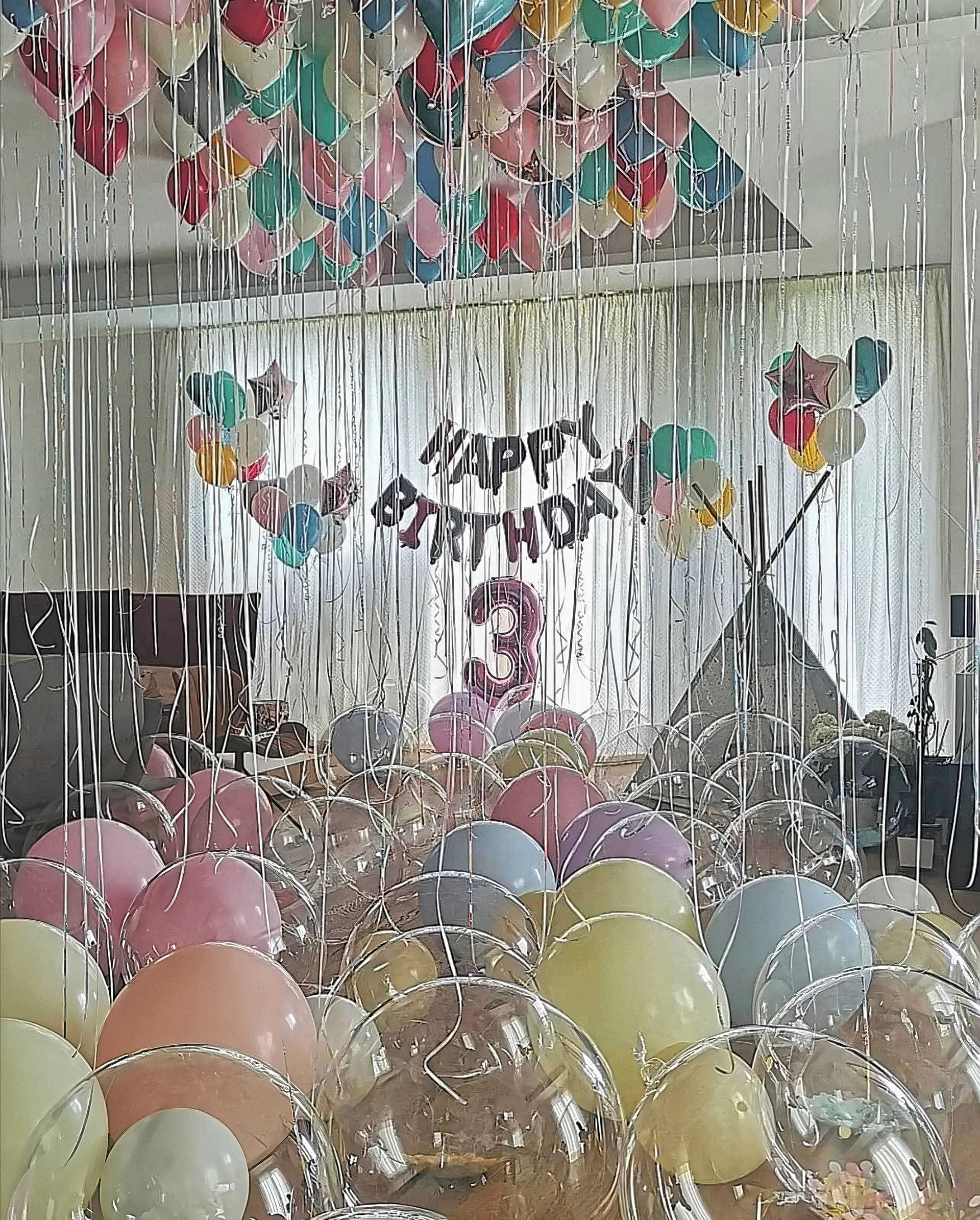 Таван, покрит с пастелни балони с дълги панделки, гирлянд Happy Birthday и цифра три